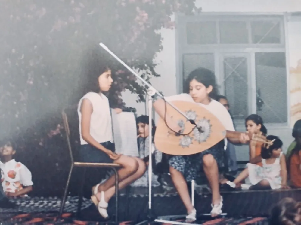 Playing the oud on stage as a child, a girl beside her holding the score